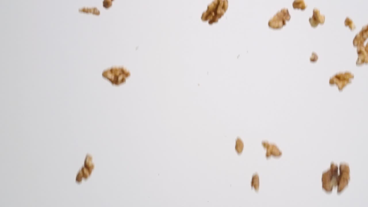 Pezzi di noci fresche, crude e marroni che cadono a pioggia su uno sfondo bianco al rallentatore