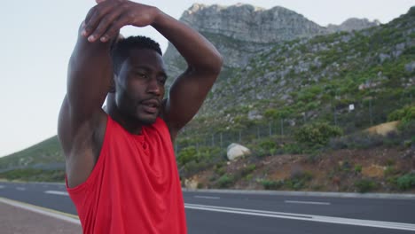 portrait of african american man wearing sports clothes and stretching on a country road