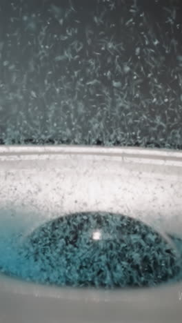 bright blue magic sand bounces from vibrations of speaker near black dust cap. loud music causes small particles to fly off surface in grey music studio macro