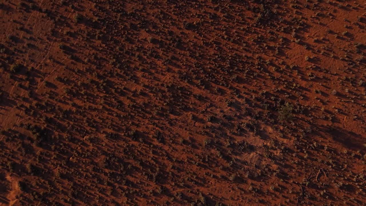 Abstract luchtpatroon van rode aarde en minimale vegetatie dat de barre omgeving van het binnenland benadrukt, drone hoog overzicht van boven naar beneden stijgend