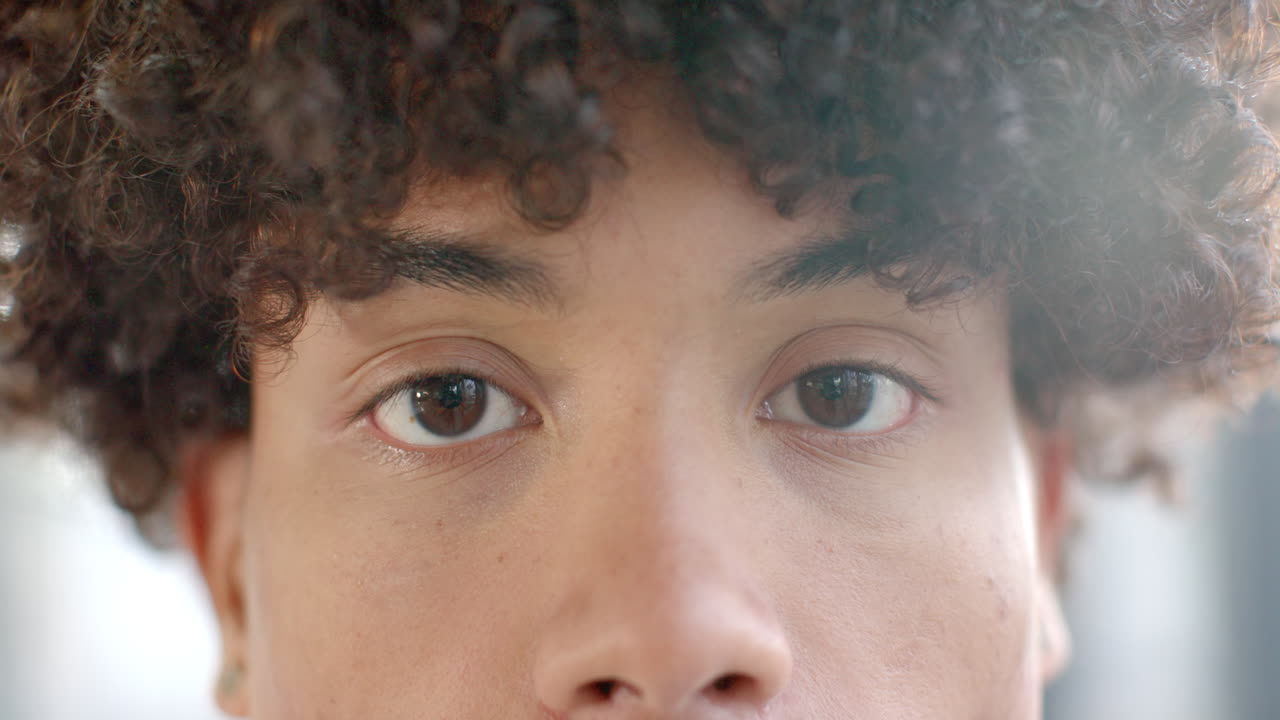 Close-up of young person's eyes with curly hair, looking directly at camera
