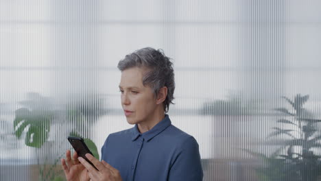 portrait-professional-senior-business-woman-using-smartphone-working-in-office-sending-emails-online-texting-messaging-on-mobile-phone-looking-pensive-concentrating-slow-motion