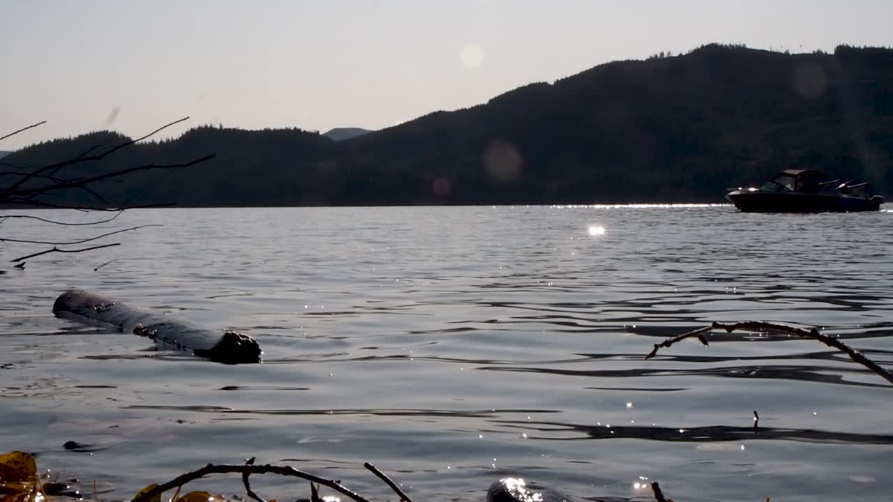 산과 렌즈 플레어가 있는 반짝이는 호수에서 보트 이동 샷의 실루엣