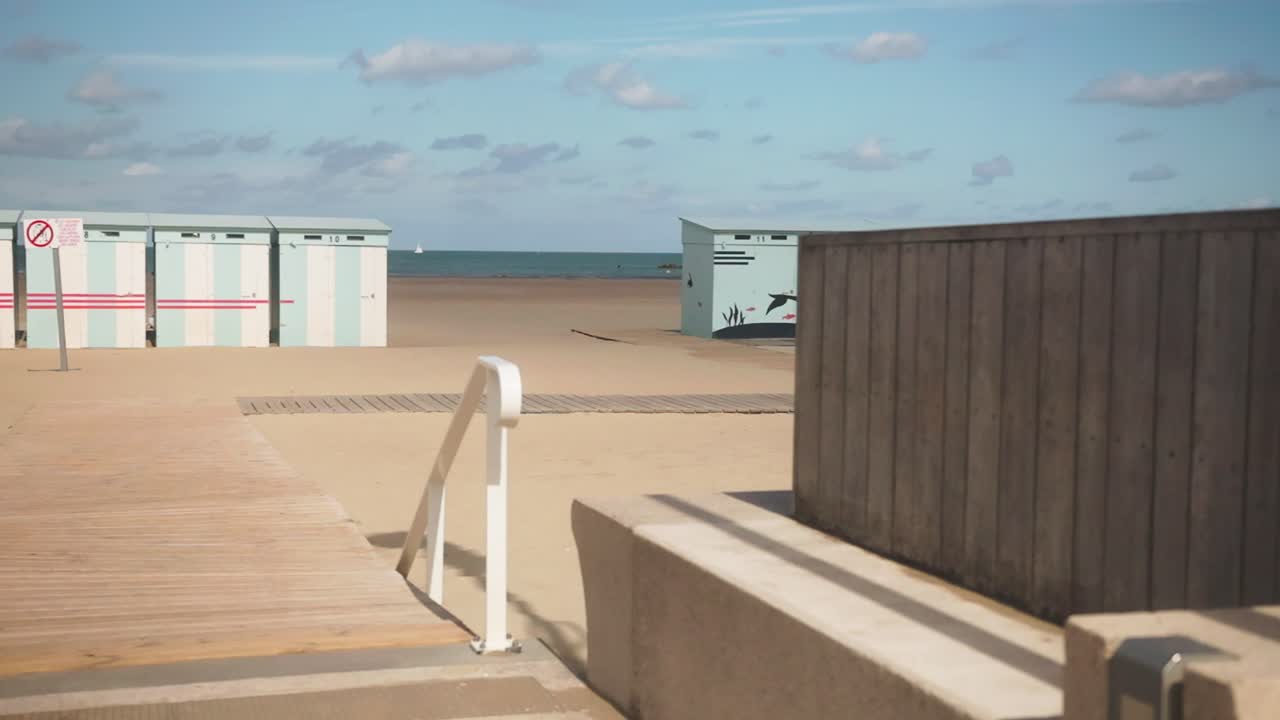 Empty sandy beach in Dunkirk with colorful cabins and boardwalk under a bright summer sky