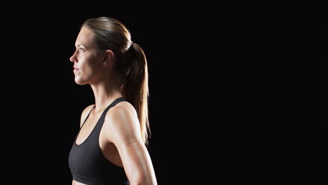 Young-Caucasian-woman-athlete-in-athletic-wear-poses-confidently-on-a-black-background,-with-copy-sp