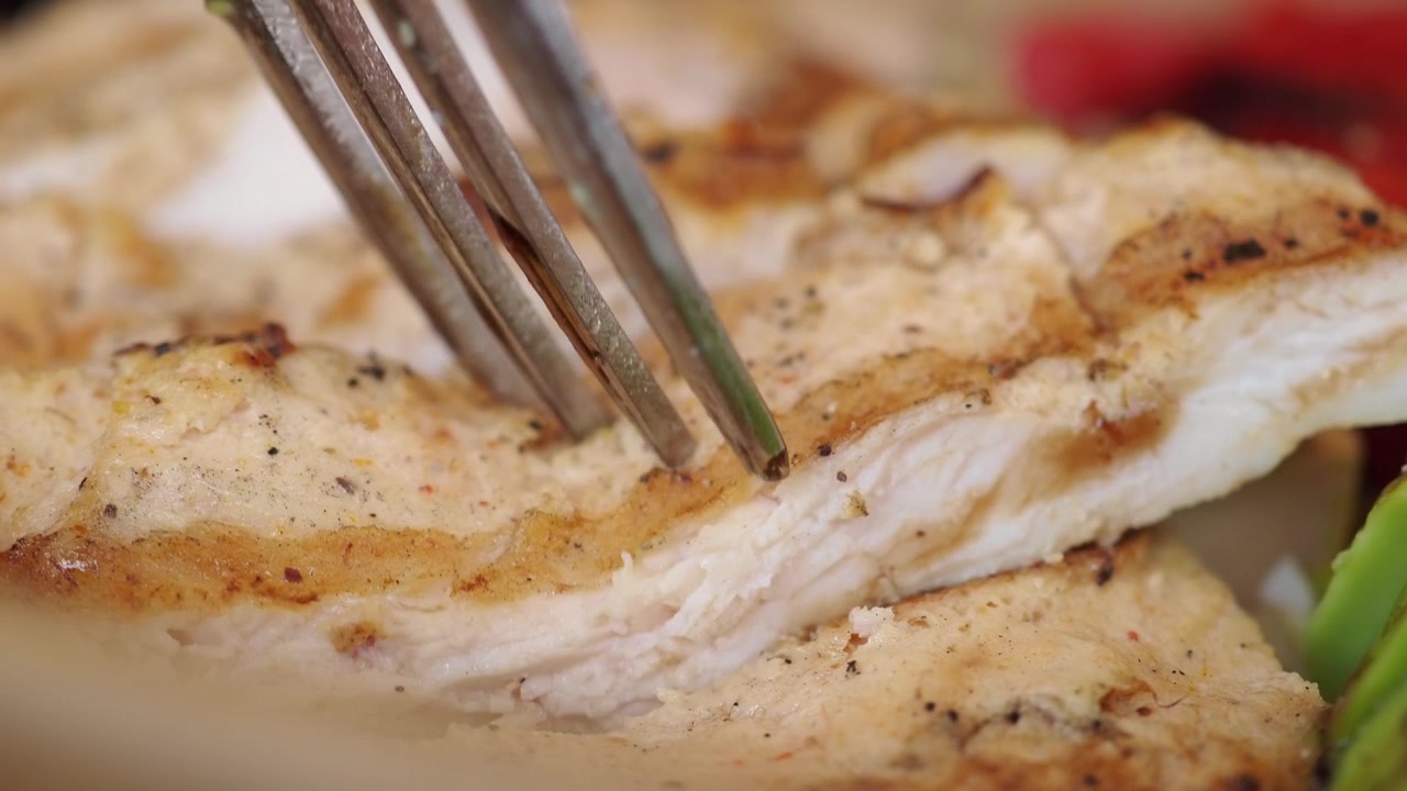 Primo piano di una forchetta che solleva un pezzo di pollo alla griglia