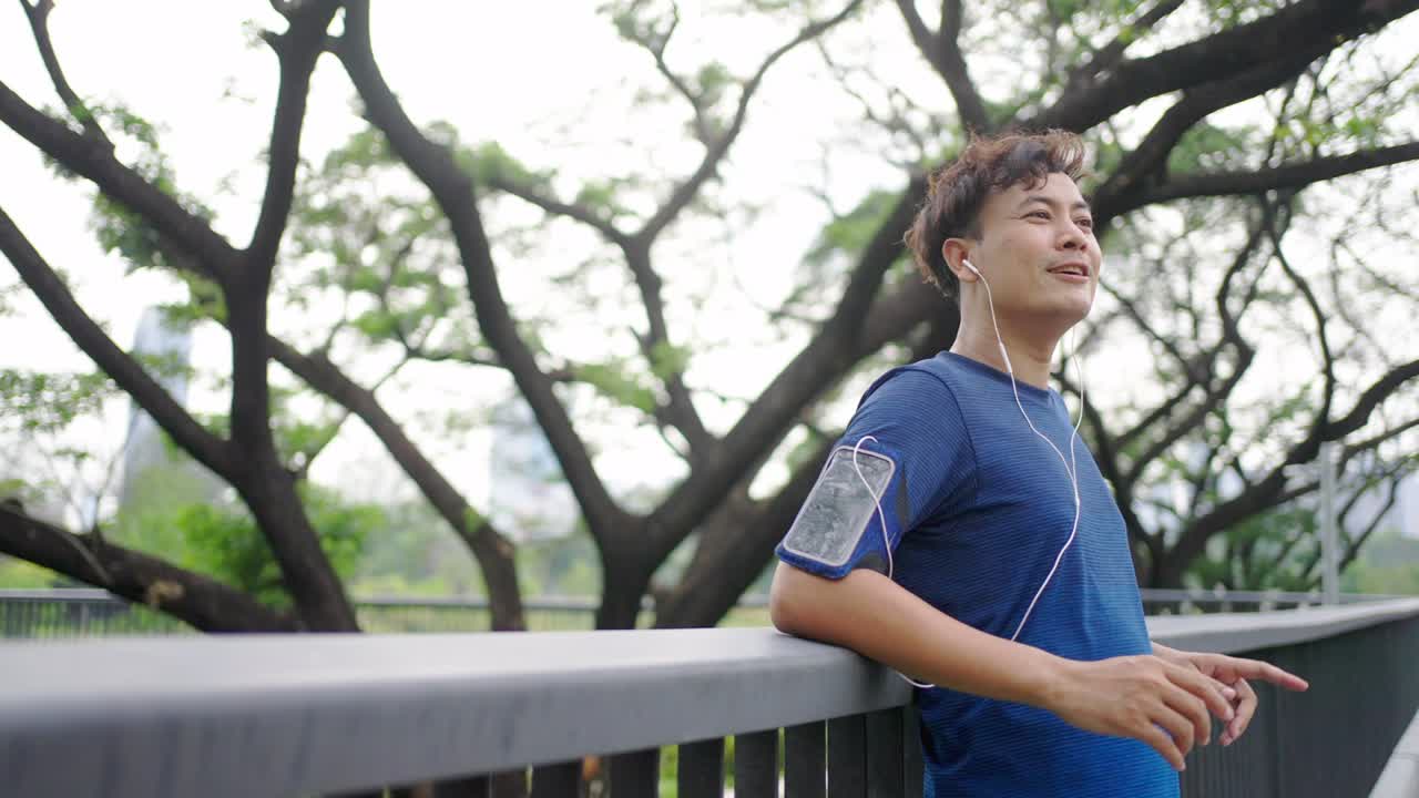 hombre asiático de 4k escuchando música mientras corre en un parque público por la mañana.