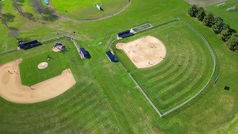 distant drone footage captures anonymous sportsmen playing baseball on vast green field, with neatly manicured grass stretching out around them