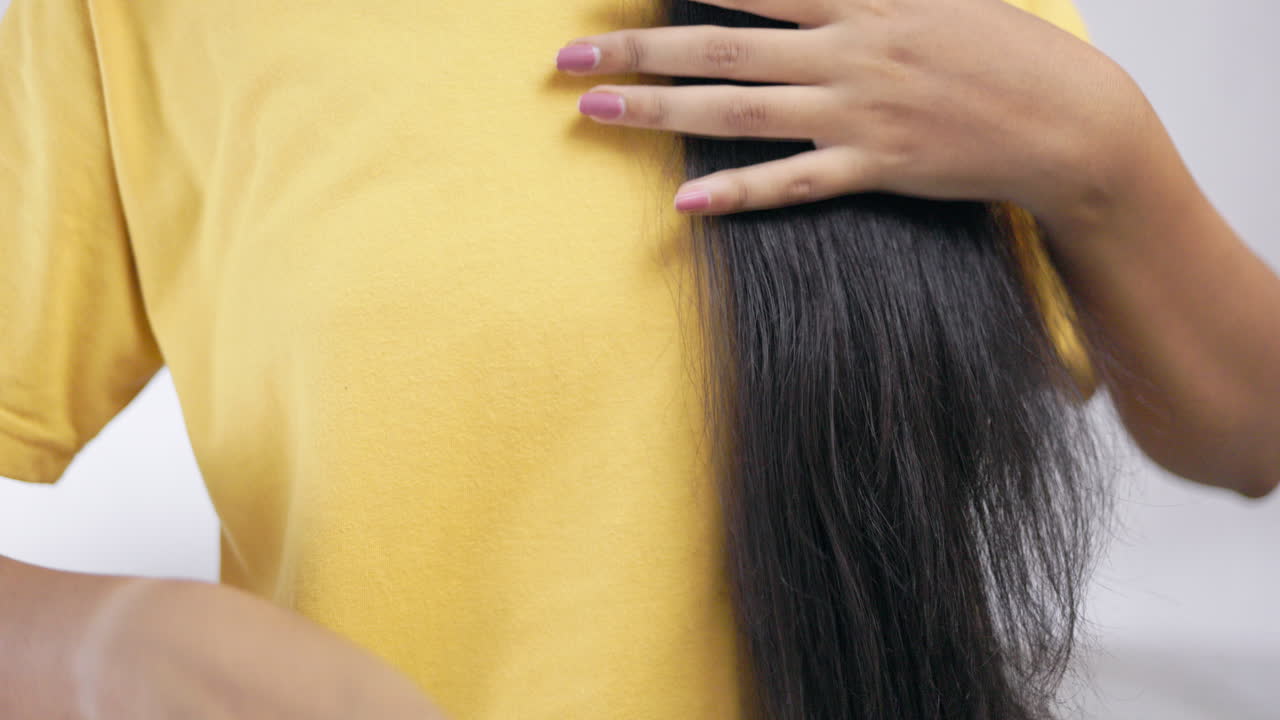 Crop view of an unrecognisable young woman combing her hair with hair brush and showing the brush in white background.