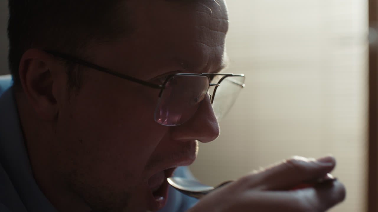 A sad man in a shirt slowly eats breakfast