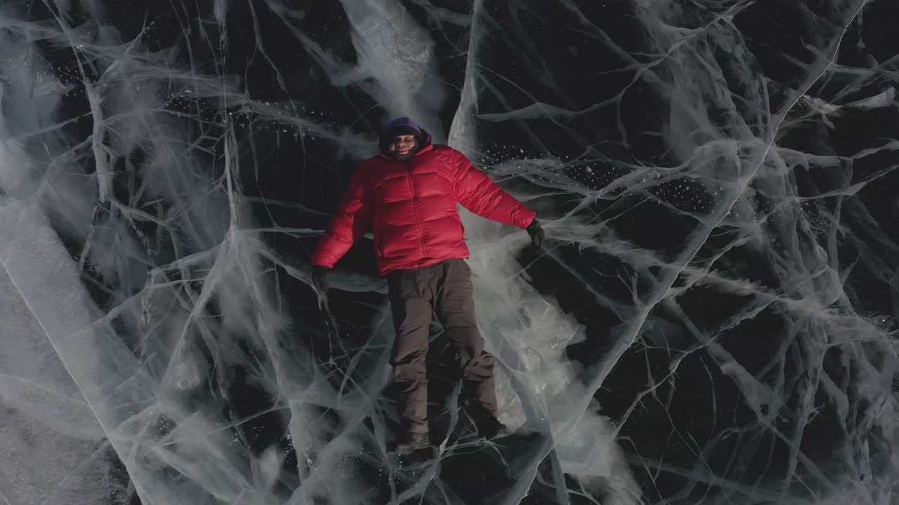 한 남자가 겨울에 얼음 위에 누워서 팔과 다리를 으로 펼쳐서 물에 떠 있는 척하고 천사를 묘사합니다.