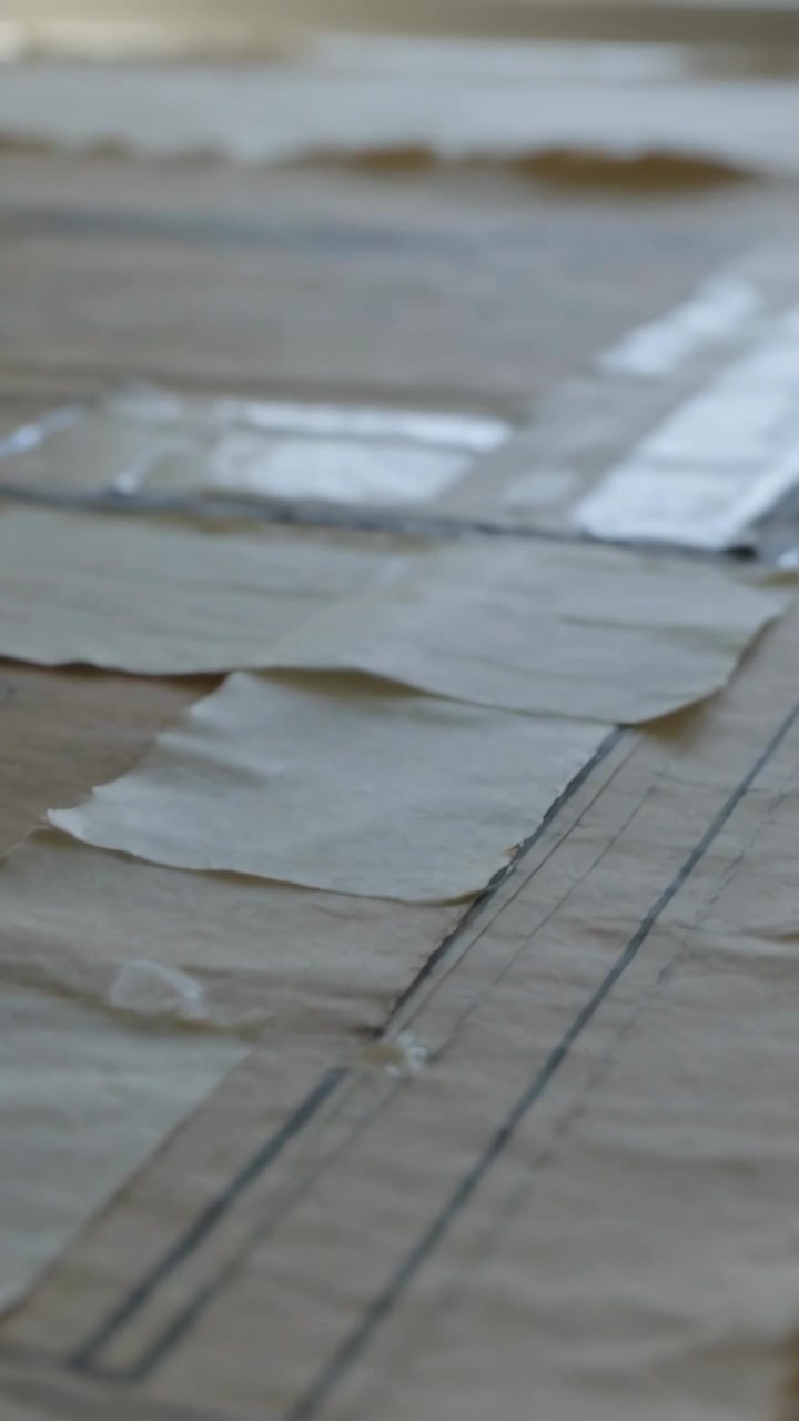 Vertical video: Panning camera revealing brown kraft pattern sheet on table, showing glue and tape