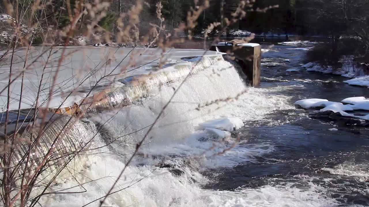 ice melting over the edge of a frozen dam. Stationary wide shot
