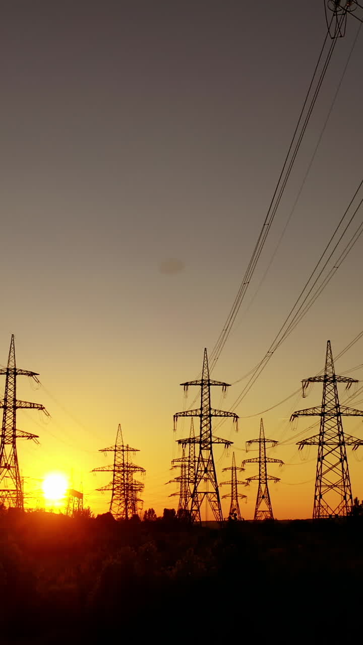 Electric towers against the orange sunset. High voltage electric lines in the evening. Silhouettes of electrical pylons. Vertical video