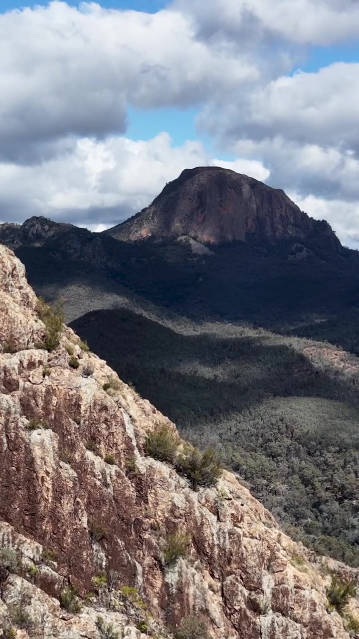 Inquadratura verticale di un'imponente cima montuosa dietro una ripida parete rocciosa di arenaria dalla texture marcata.