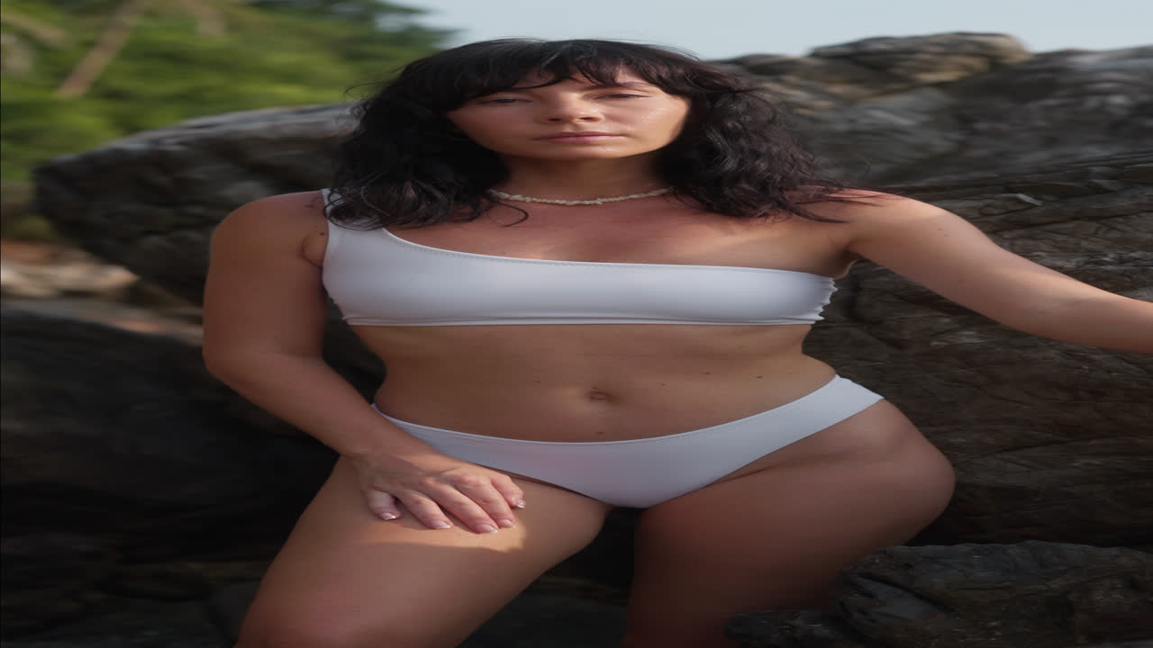 Giovane donna in bikini bianco in posa su spiaggia rocciosa