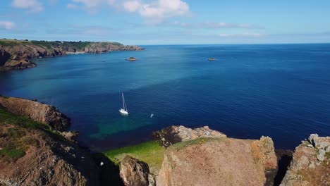 exploring the rocky island of sark by drone where many seagulls fly over an isolated sailing ship