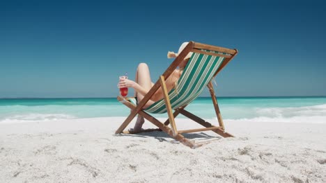 Woman-drinking-cocktail-on-deck-chair-on-the-beach