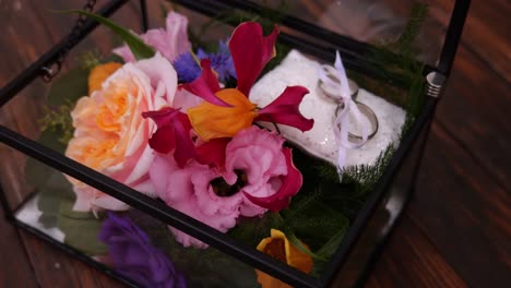 caja transparente abierta con flores y anillos de boda