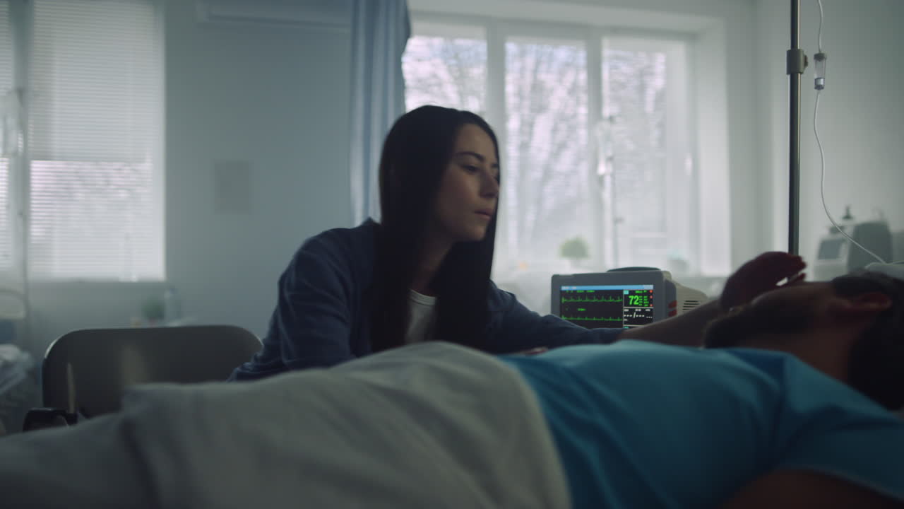 Hospital visitor supporting patient stroking face. Modern clinic ward interior.