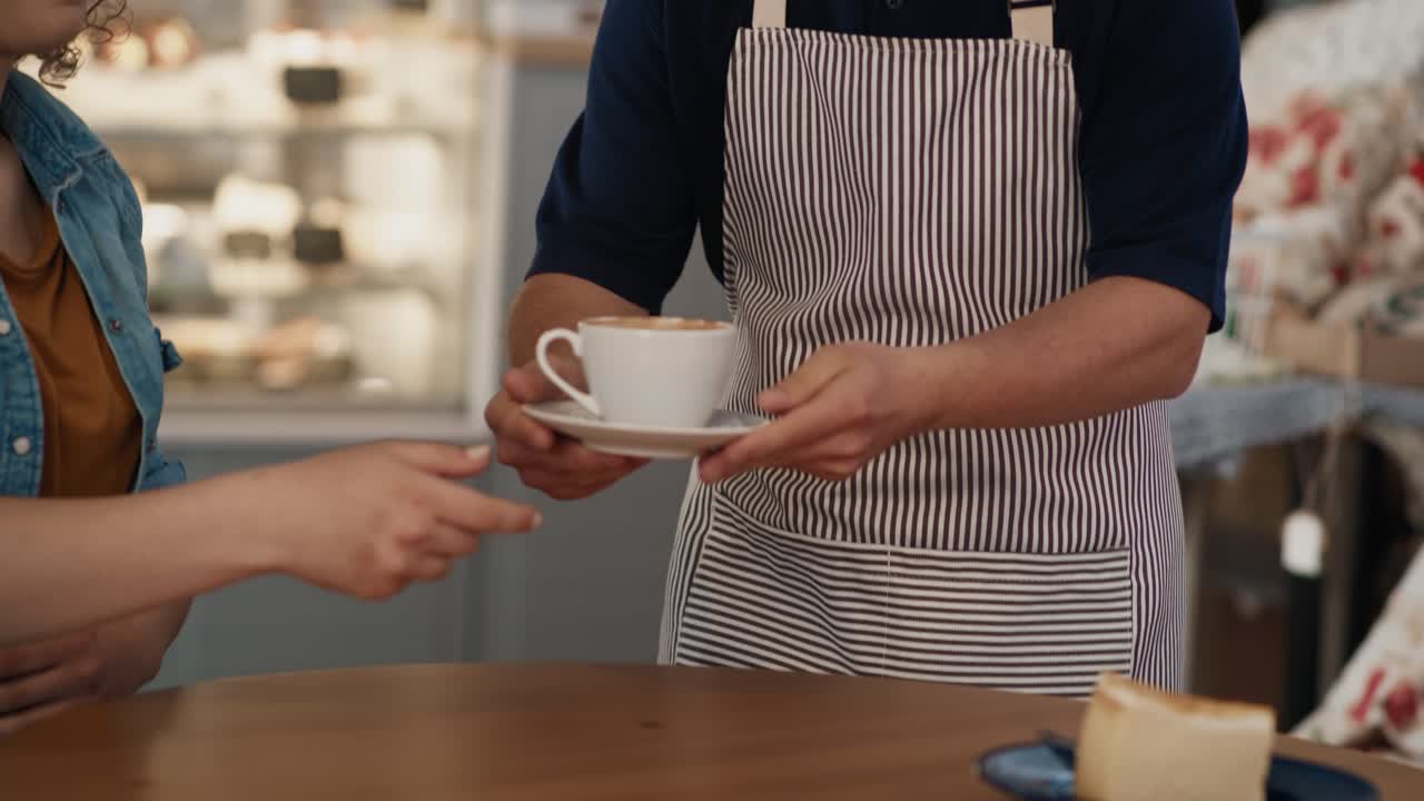 Caucasian male waiter with down syndrome serving a cup of coffee in the cafe to the client at the table.