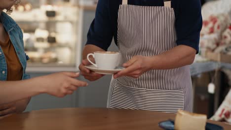 Caucasian-male-waiter-with-down-syndrome-serving-a-cup-of-coffee-in-the-cafe-to-the-client-at-the-table.