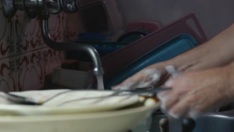 mans hands washing dishes in kitchen sink with soapy sponge medium shot
