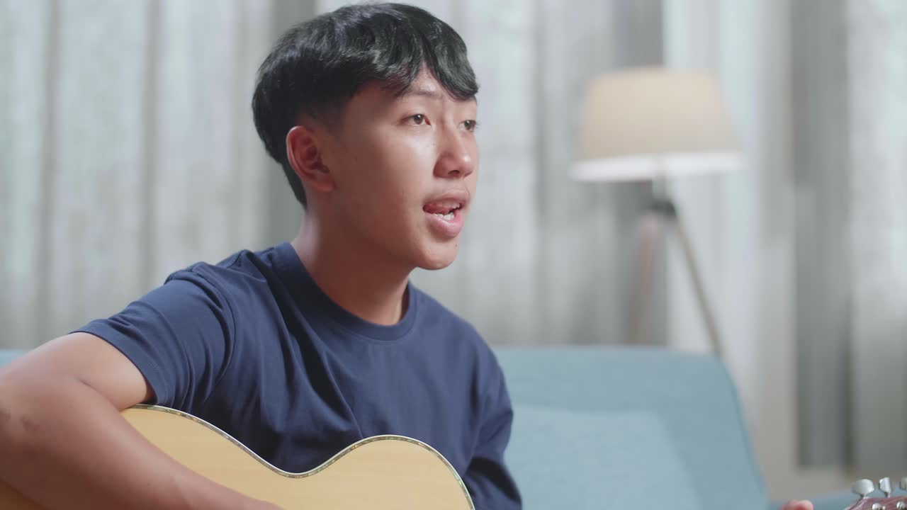 테이블 위에 노트북을 들고 집에서 노래하고 기타를 연주하는 아시아 소년 작곡가의 클로즈업