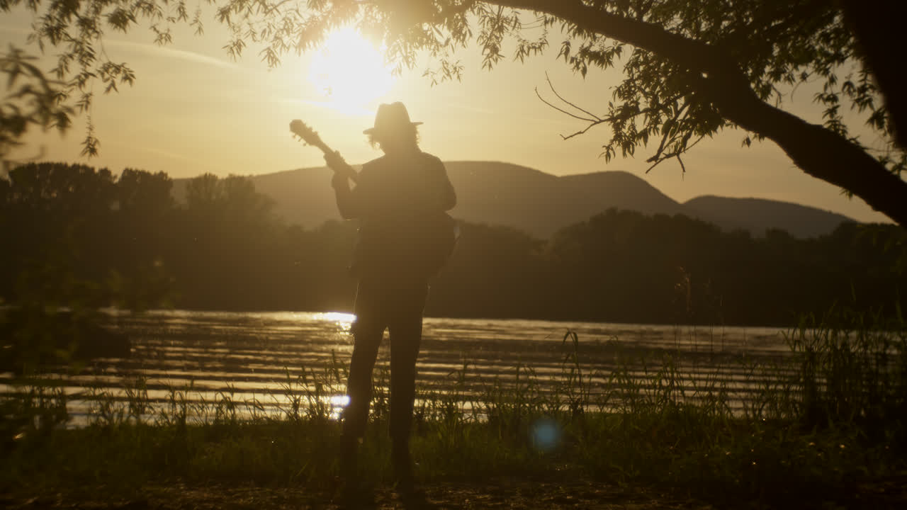 Silhouette of a Musician Playing Guitar at Sunset by the River