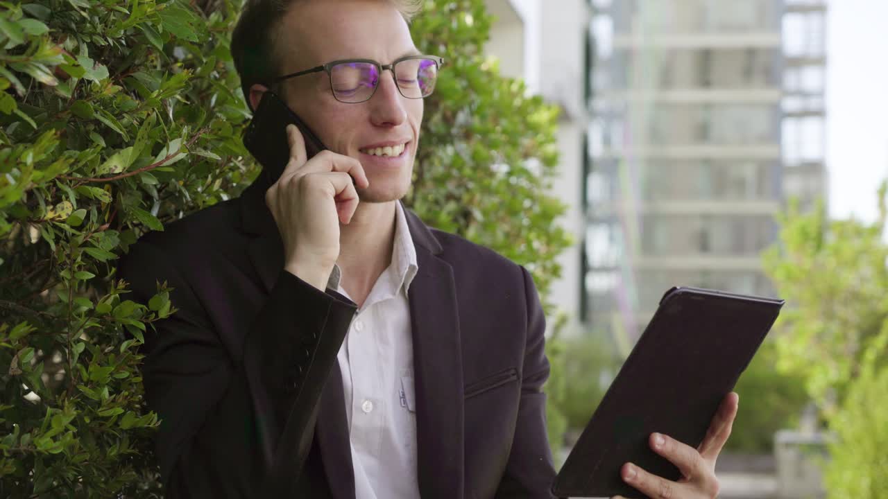 hombre de pie afuera, hablando por teléfono, mirando la tableta