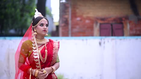 reflexiva novia india bengalí sonriendo y esperando al aire libre vistiendo sari rojo