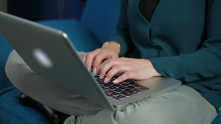 Eine unkenntliche Frau arbeitet im Schneidersitz auf einem Sofa am Laptop.