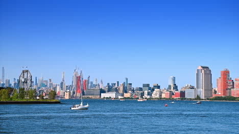 sailboat moves by the waterscape of the hudson river. vast skyline of new york downtown at backdrop
