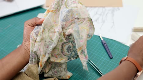 vista superior de la mujer sastre sentada en la mesa eligiendo hilo para piezas de ropa en el taller de costura