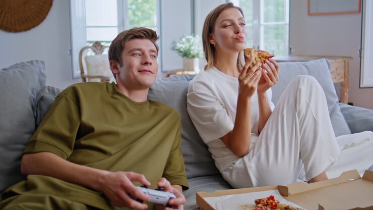 Amici affamati si godono una cena casalinga davanti alla TV in primo piano. Giovani che scelgono un videogioco