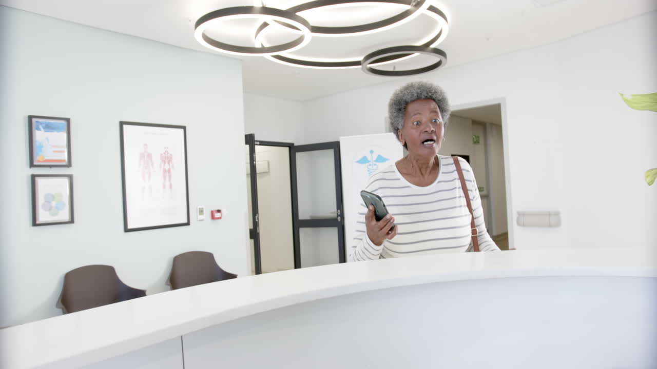 African american senior woman with smartphone talking in hospital reception, slow motion