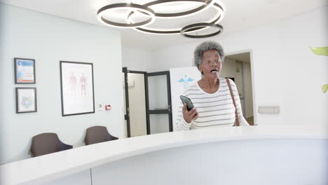 afrikanisch-amerikanische ältere frau mit smartphone spricht in der krankenhausrezeption, slowmotion