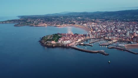 Vista-Aérea-De-Gijón-En-La-Capital-De-Galicia-Durante-La-Noche,-El-Centro-De-La-Ciudad-Y-El-Puerto-Iluminados