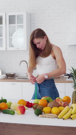 attractive girl with meter in the kitchen. fresh organic food on the table. young woman is measuring her waist at home. concept of losing weight. vertical video