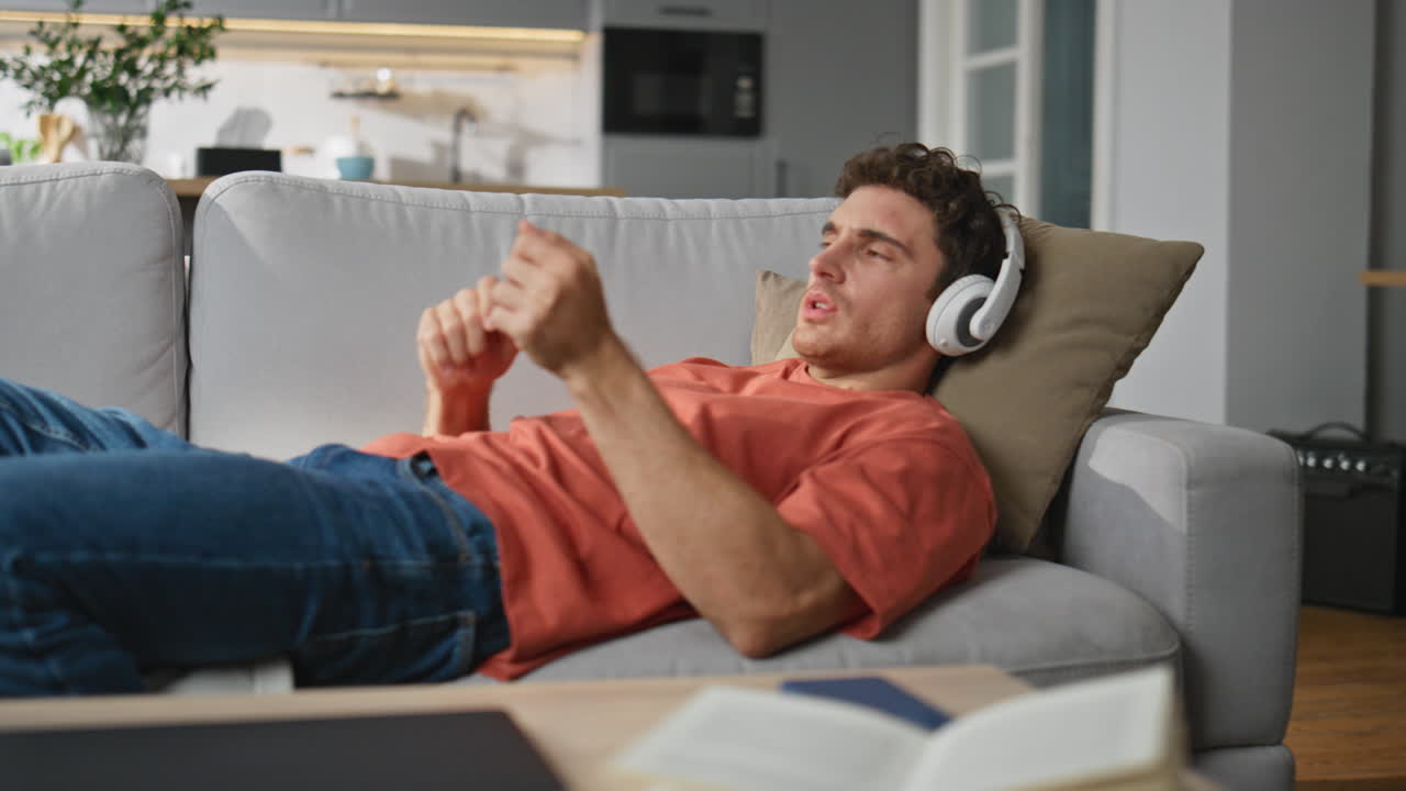 Relaxed guy listening headphones music at sofa closeup. Man moving in song beat