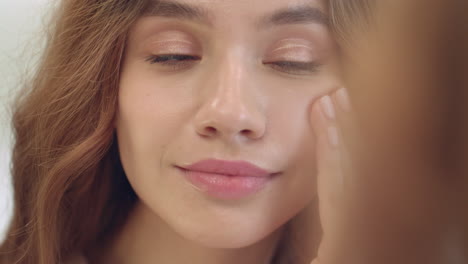 smiling woman applying moisturizing cream on face skin