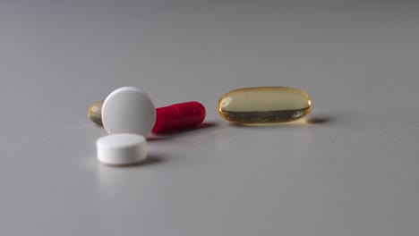 white round vitamin tablet roll on grey table and stop near other pills