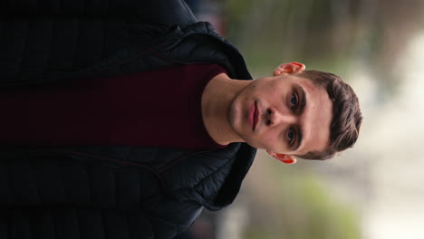 video vertical, retrato de un apuesto joven modelo masculino, vestido con ropa casual, mirando a la cámara, aspecto neutral, al aire libre