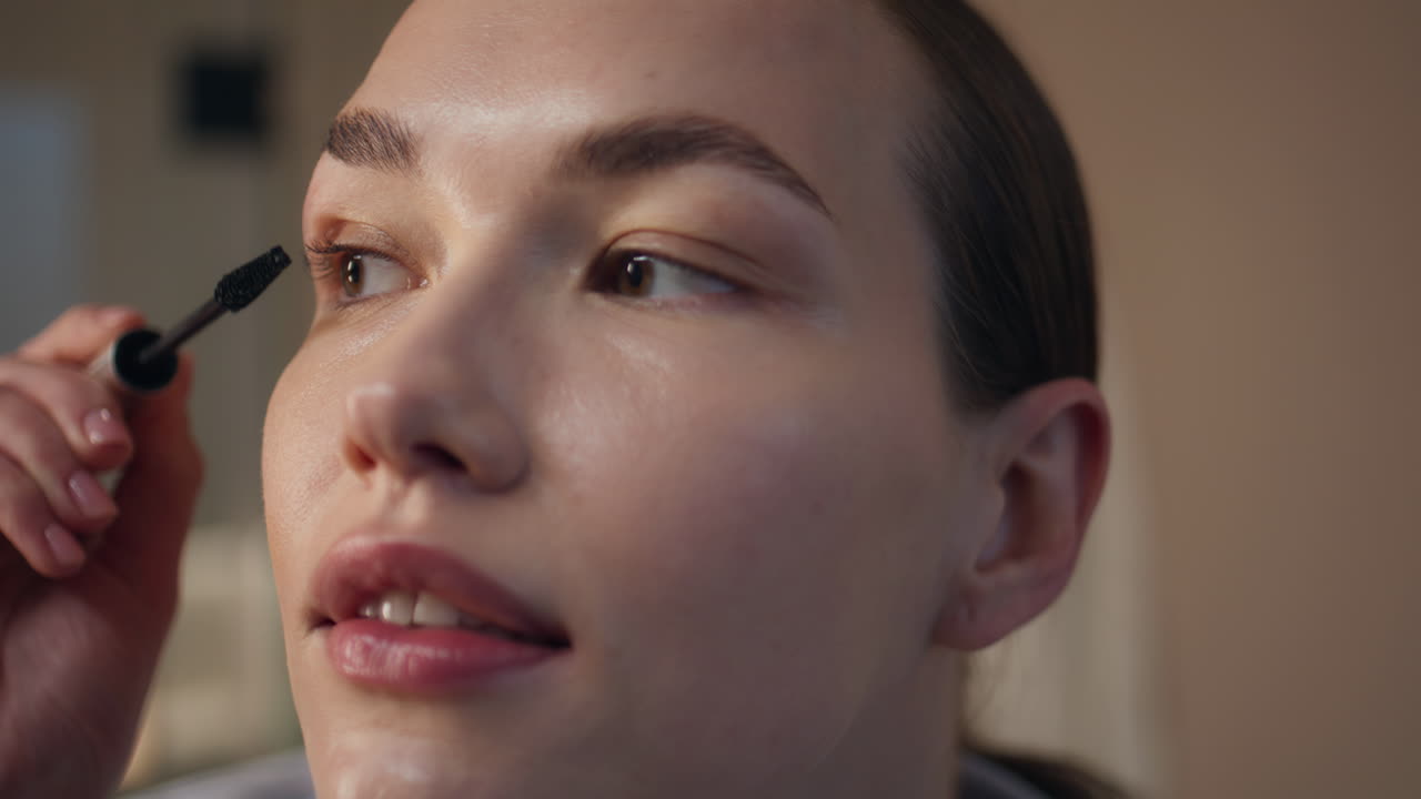 Beauty girl putting makeup in evening light. Closeup relaxed lady apply mascara