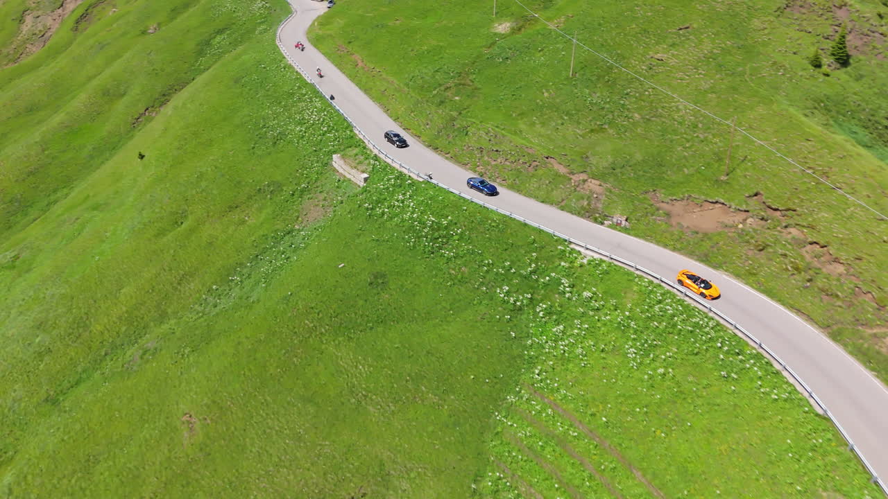 Aerial drone view of sleek performance cars driving along winding alpine serpentine road in summer mountains with forest and clouds