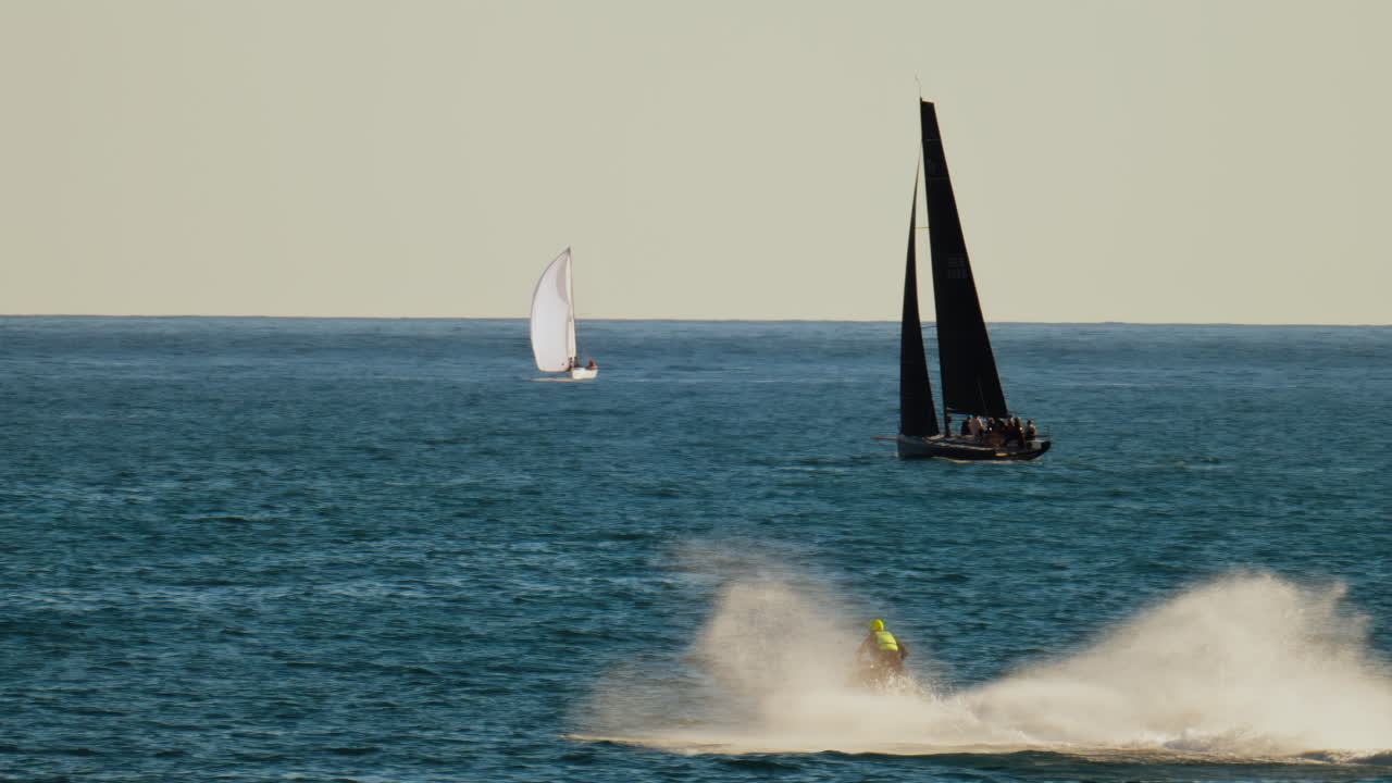 Man on a jet ski moving on the sea near multiple sailboats