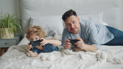 father and son playing video games on bed