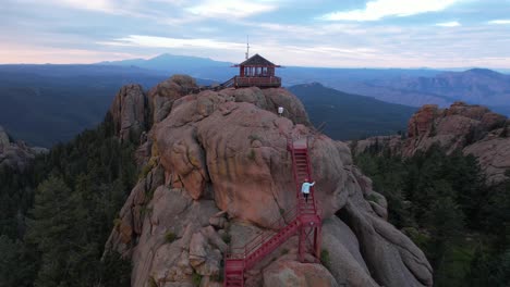 Aerial-View-of-Woman-Walking-on-Stairways-on-Top-of-Mountain-Peak-to-Hilltop-Cottage,-Devil's-Head,-Colorado-USA