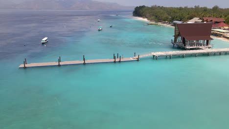 Nach-Unten-Geneigte-Luftaufnahme-Einer-Person,-Die-An-Einem-Sommertag-Auf-Der-Insel-Gili-Auf-Einem-Steg-Läuft-Und-Im-Hintergrund-Boote-Parkt