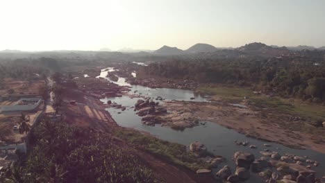 tungabhadra river flow cascading alongside the rocky landscape hampi town's edge in karnataka, india - aerial fly-over